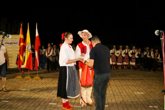 Para tancerzy w polskich strojach ludowych wręczająca mężczyźnie podarunek na scenie