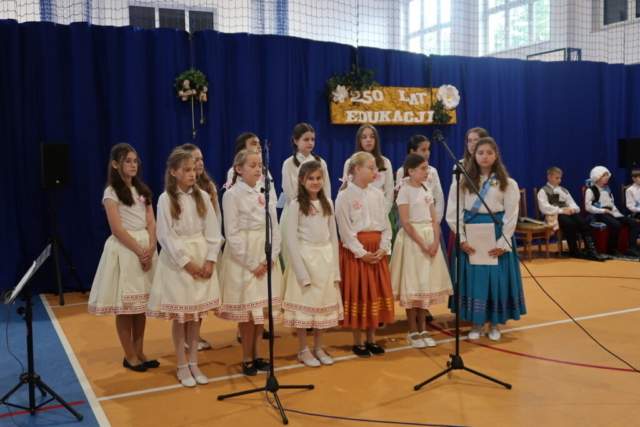 Szkolny zespół wykonuje utwór "Laura i Filon". Dzieci stoją na tle dekoracji okolicznościowej.