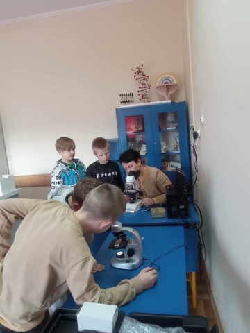 Czterech chłopców i nauczyciel są przy stolikach. Patrzą przez mikroskopy.