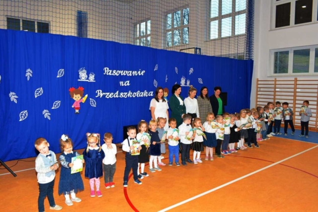 Dzieci z najmłodszej grupy przedszkolnej "Słoneczka" stoją trzymając dyplomy pasowania. Za nimi panie wychowawczynie, Dyrektor Szkoły oraz Wójt Gminy Dydnia..