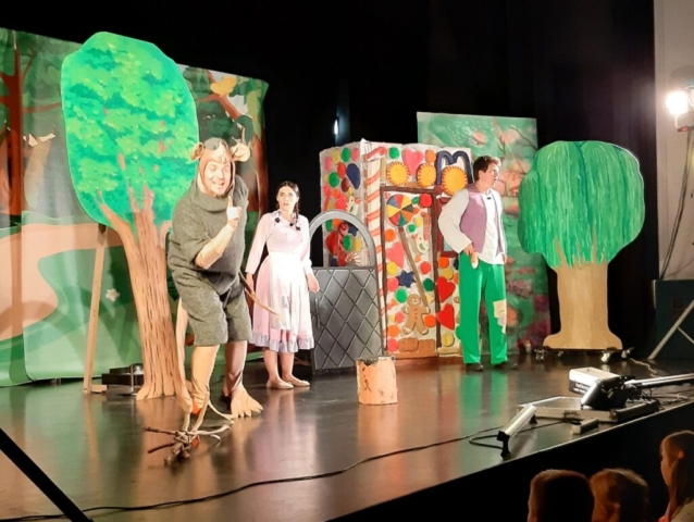 Na scenie, na tle dekoracji lasu i domku czarownicy troje aktorów wcielających się w postać Jasia, Małgosi i szczura odgrywa scenę z baśni