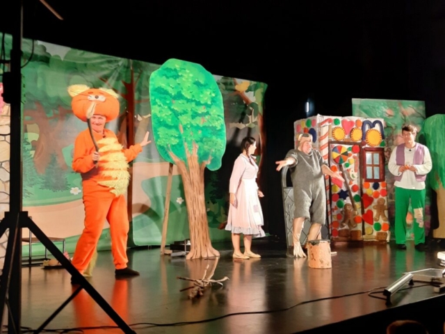 Na scenie, na tle dekoracji lasu i domku czarownicy czworo aktorów wcielających się w postać kota, Jasia, Małgosi i szczura odgrywa scenę końcową z baśni