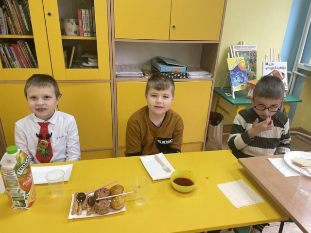 Spotkanie wigilijne klasy I - trzech chłopców przy stole częstuje się słodkościami.