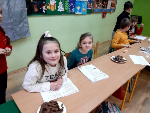 Wigilia klasy II . Dzieci siedzą przy wspólnym świątecznym stole i częstują się słodkościami.