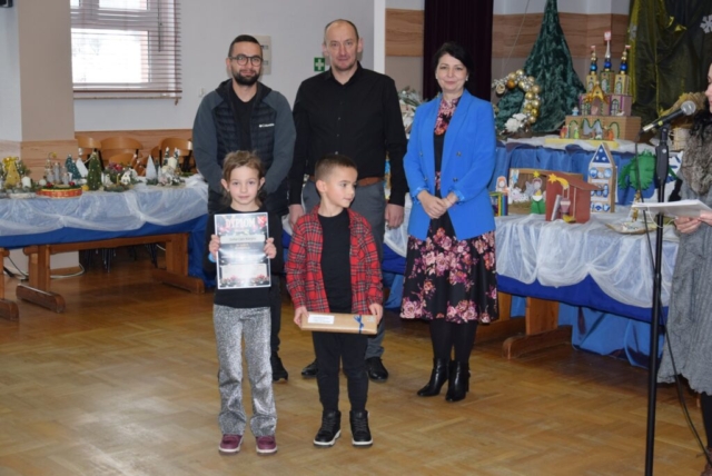 Dzieci wraz z rodzicem otrzymały dyplom i nagrodę z rąk p. wójt i dyrektora GOK za najpiękniejszą szopkę/ stroik bożonarodzeniowy. W tle ozdoby bożonarodzeniowe