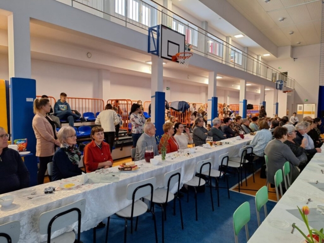 Dziadkowie oraz zaproszeni goście siedzą przy wspólnych stołach na sali gimnastycznej