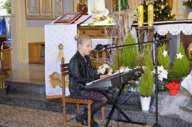 Dziewczynka siedzi przed keyboardem, gra i śpiewa kolędę, w tle wnętrze kościoła ze świąteczną dekoracją
