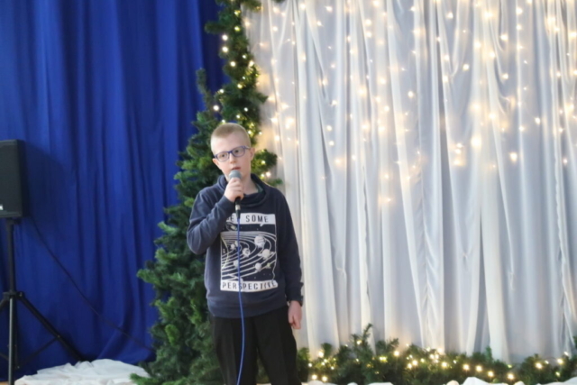 Chłopiec stoi na tle dekoracji, trzyma mikrofon i śpiewa