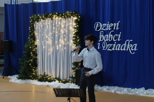 Uczeń stoi z mikrofonem na tle dekoracji i wykonuje piosenkę,