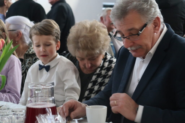 Dziadek z babcią siedzą wraz z wnukiem przy stole