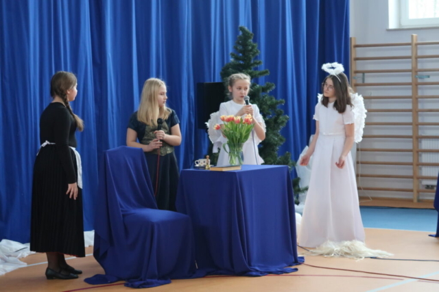 Cztery dziewczynki w rolach służących, anioła i hrabiny odgrywają scenkę wspólnej rozmowy. W tle okolicznościowa dekoracja