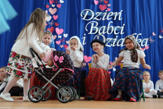 Dziewczynki z najstarszej grupy przedszkolnej odgrywają wesoła scenkę, występują w przebraniach babć oraz mamy z wózkiem