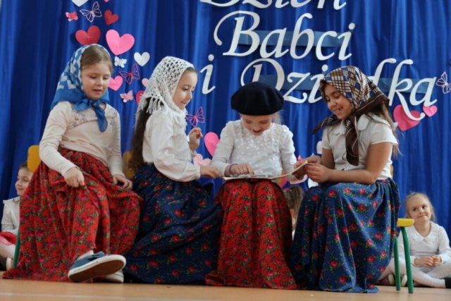 Dziewczynki z najstarszej grupy przedszkolnej odgrywają wesoła scenkę, występują w przebraniach babć