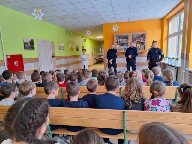 Dyrektor szkoły przedstawia dzieciom policjantów przybyłych na prelekcję