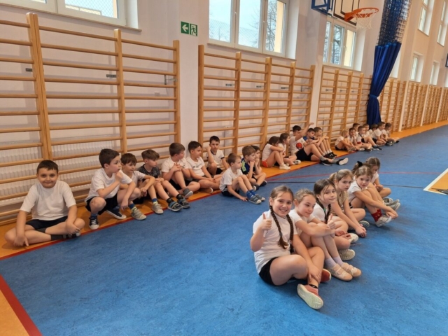 Dzieci ubrane w stroje sportowe. siedzą na sali gimnastycznej w oczekiwaniu na rozgrywki