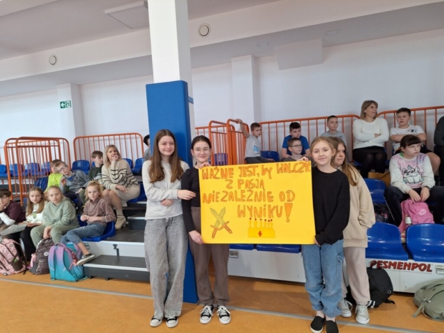 Dzieci na trybunach kibicują kolegom, Dziewczynki trzymają plakat z zachętą do walki sportowej swojej klasy