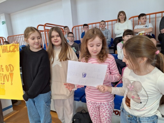 Dzieci na trybunach kibicują kolegom, Dziewczynki trzymają plakaty z zachętą do walki sportowej swojej klasy
