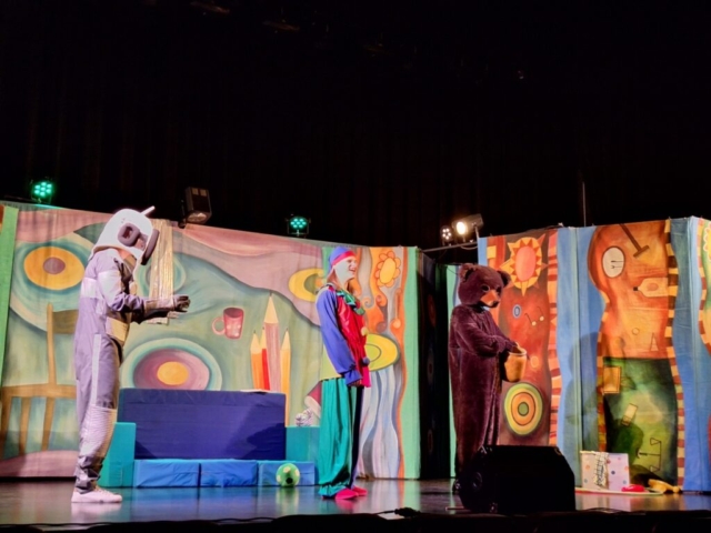 Troje aktorów na scenie odgrywa rolę misia, pajacyka i robota. W tle barwna dekoracja przedstawiająca dziecięcy pokój