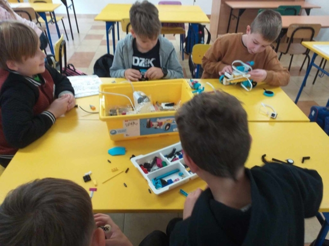 Uczniowie siedzą w ławkach szkolnych i budują konstrukcje za pomocą klocków Lego