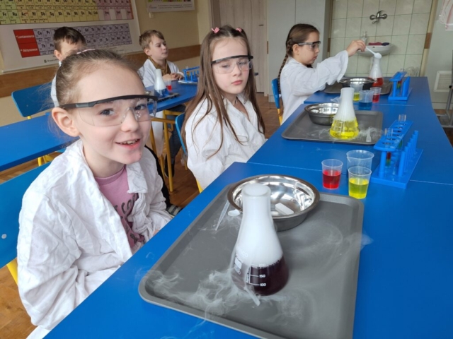 Dzieci wykonują doświadczenia chemiczne pod kontrolą osoby prowadzącej i nauczycieli
